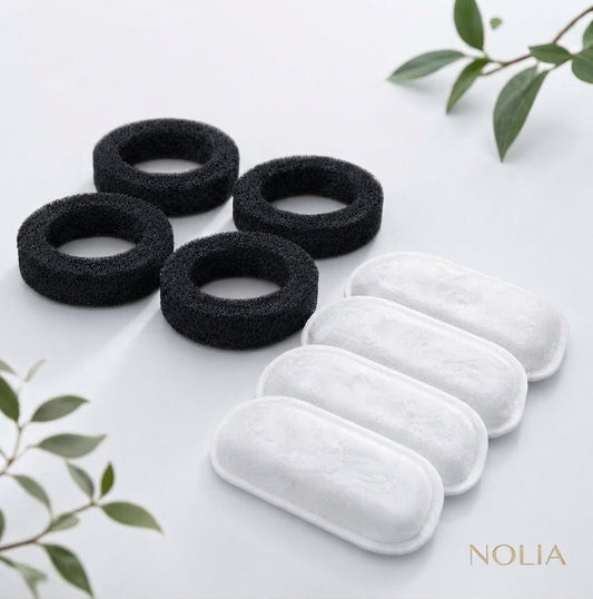Lot de recharges pour fontaine à eau Nolia comprenant quatre filtres en mousse noire de pré-filtration et quatre filtres blancs haute pureté, présentés sur un fond épuré avec des touches de feuillage.