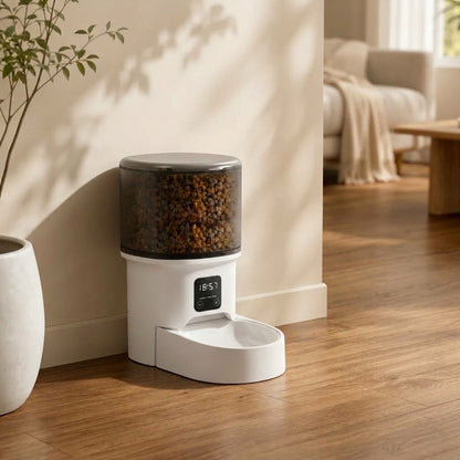 Distributeur automatique de croquettes blanc avec réservoir transparent et écran digital, posé sur un parquet dans un salon moderne.